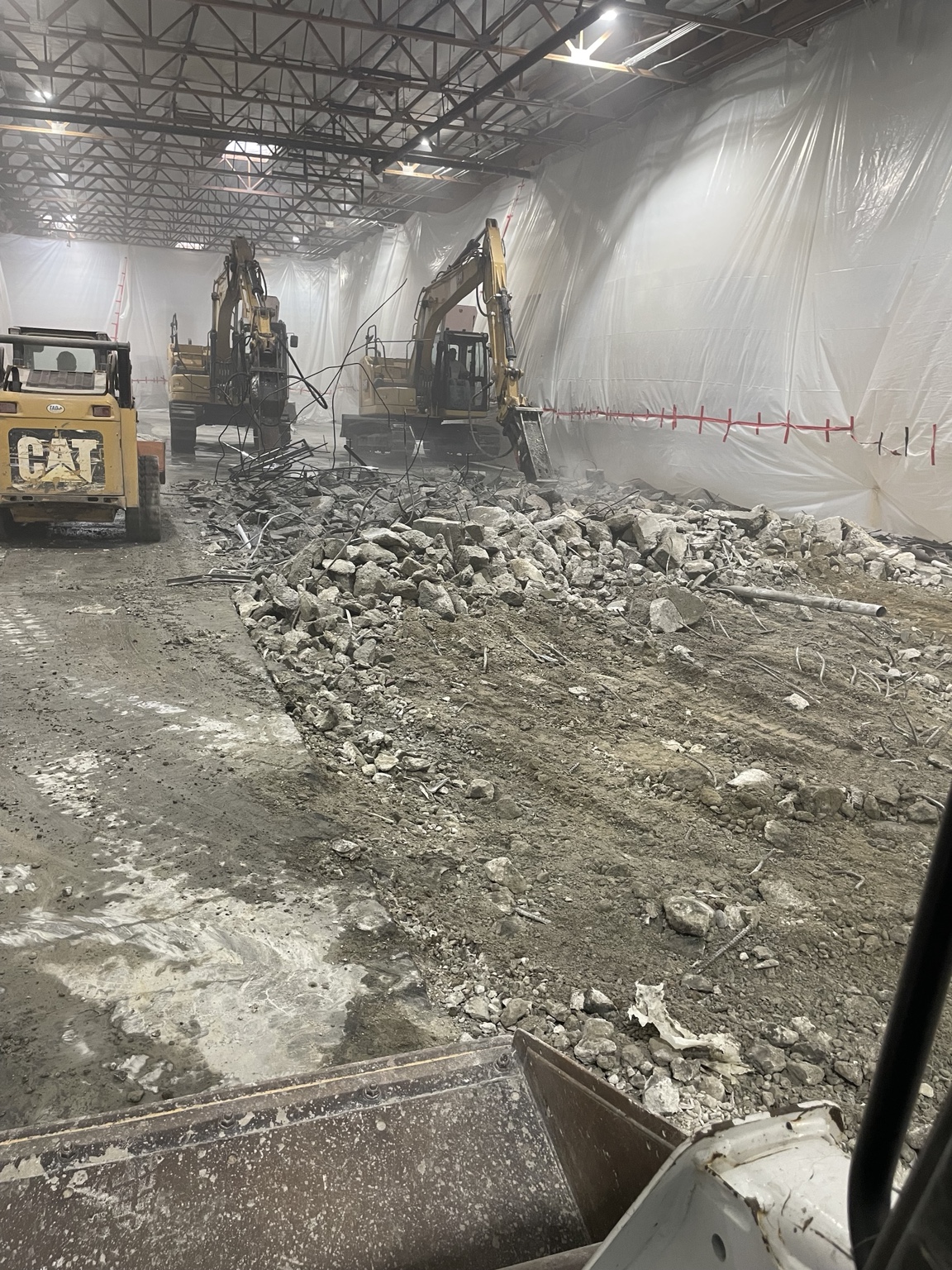 Excavators breaking and removing an existing concrete slab inside visqueen containment