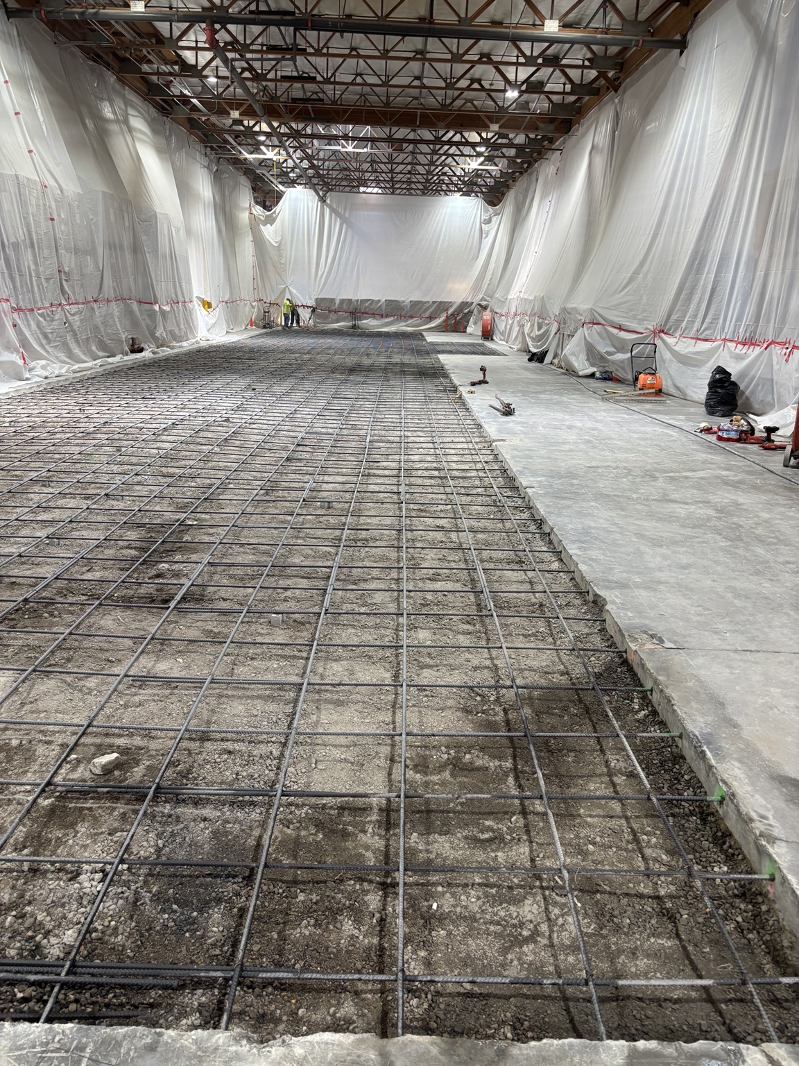 Reinforcing steel installed over the prepared base for the replacement slab, with the work area enclosed in visqueen